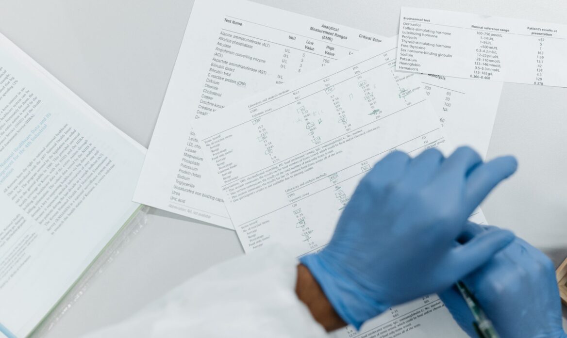 Osoba w niebieskich rękawiczkach analizująca wyniki badań medycznych na papierze.