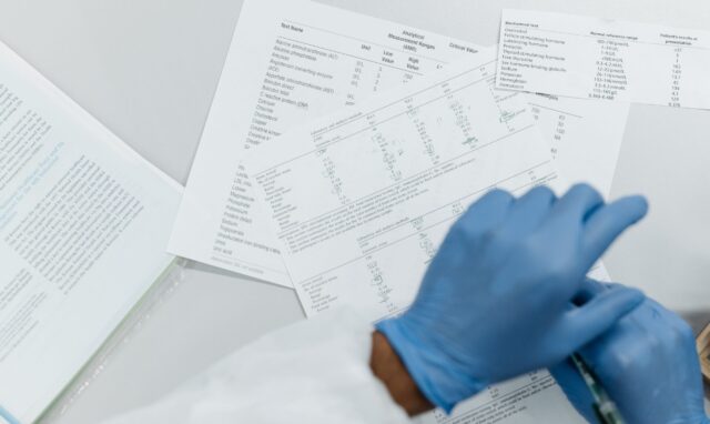 Osoba w niebieskich rękawiczkach analizująca wyniki badań medycznych na papierze.